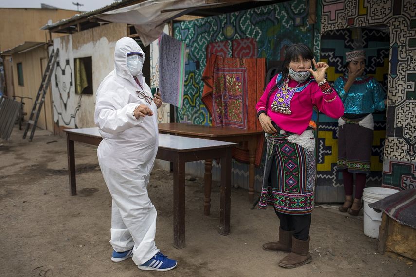 Olinda Silvano, de la etnia shipibo conibo, habla con una trabajadora de una ONG ataviada con ropa de protecci&oacute;n contra el nuevo coronavirus, durante las celebraciones del d&iacute;a de San Juan, santo patr&oacute;n de la Amazon&iacute;a peruana, en el barrio de Cantagallo, en Lima, Per&uacute;, el mi&eacute;rcoles 24 de junio de 2020. (AP Foto/Rodrigo Abd