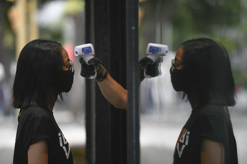Un empleado de una tienda le toma la temperatura a una mujer como precaución contra el coronavirus el sábado 25 de julio de 2020, en Caracas, Venezuela. 