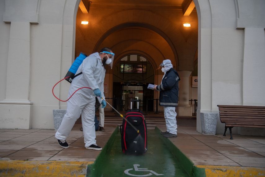 Un empleado en traje de protecci&oacute;n desinfecta el equipaje de un pasajero frente a la terminal de la empresa argentina de servicios de ferry Buquebus en el puerto de Montevideo, el 10 de julio de 2020, en medio de la nueva pandemia de coronavirus.