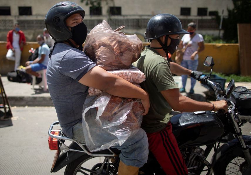 Dos hombres, con mascarillas para protegerse del coronavirus, transportan bolsas de carne y salchichas sobre una motocicleta el mi&eacute;rcoles 8 de julio de 2020 en un mercado callejero, en Caracas, Venezuela.