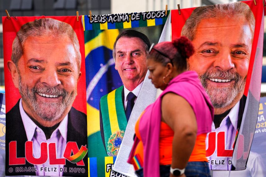 Una mujer pasa junto a toallas adornadas con imágenes de los candidatos presidenciales brasileños, el presidente Jair Bolsonaro, al centro, y el expresidente Luiz Inácio Lula da Silva, que un vendedor ambulante pone a la venta en un tendedero improvisado en Brasilia, Brasil.