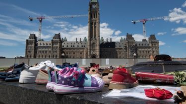 Zapatos, letreros y tabaco son colocados frente al Parlamento, en Ottawa, Ontario, el lunes 31 de mayo de 2021, en reconocimiento al descubrimiento de los cadáveres de decenas de niños en el sitio de un antiguo internado en Kamloops, Columbia Británica.