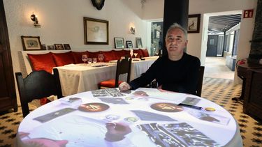 El chef español Ferran Adria posa sentado en una mesa con proyecciones de video en el antiguo comedor del restaurante El Bulli transformado en Museo elBulli1846 durante una entrevista con AFP, en Roses, cerca de Barcelona, el 24 de mayo de 2023.&nbsp;