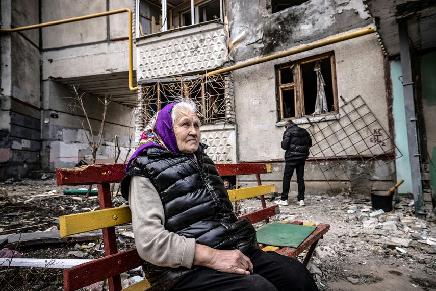 Una mujer mira mientras se sienta en un banco frente a un edificio destruido en la ciudad de Kharkiv, en el este de Ucrania, el 2 de abril de 2022.