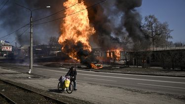 Un hombre huye con sus pertenencias mientras el fuego envuelve un vehículo y un edificio tras el fuego de artillería en el día 30 de la invasión de Ucrania por las fuerzas rusas en la ciudad nororiental de Kharkiv el 25 de marzo de 2022.