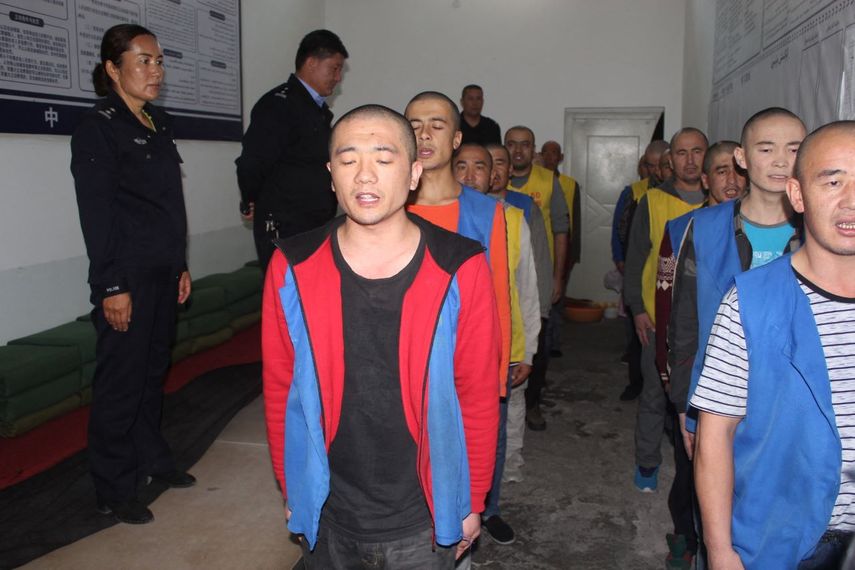 La Fundación Conmemorativa de las Víctimas del Comunismo muestra a los detenidos custodiados por la policía mientras hacen fila aparentemente recitando o cantando en el centro de detención del condado de Tekes en la región de Xinjiang, en el oeste de China.