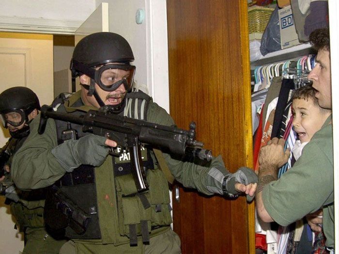 Elián González es retenido en un armario por Donato Dalrymple, uno de los dos hombres que rescataron al niño del océano, a la derecha, mientras funcionarios del gobierno registran la casa de Lázaro González en busca del niño en Miami, Florida, el 22 de abril de 2000.&nbsp;