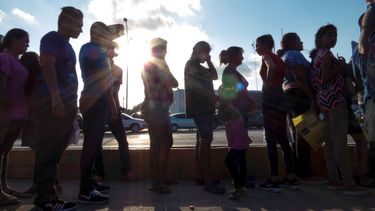 En esta fotografía de archivo del 5 de octubre de 2019, varios migrantes que desean asilo en Estados Unidos hacen fila con sus documentos en el campo para migrantes afuera de El Puente Nuevo, en Matamoros, México. 