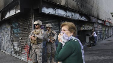 Una mujer cubre su boca para protegerse del polvo cuando soldados armados montan guardia en una esquina incendiada en Santiago, Chile, el s&aacute;bado 26 de octubre de 2019.&nbsp;