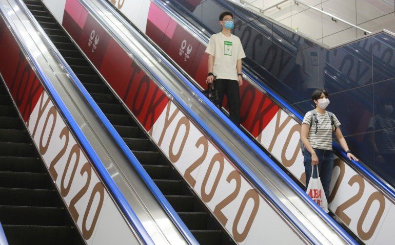 un par de personas con mascarillas baja por elevador con banderas con el logo de los Juegos Olímpicos en Tokio