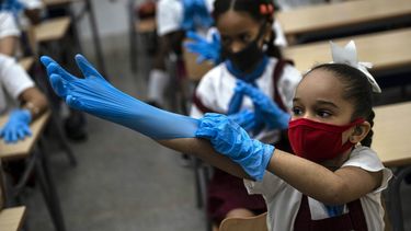 Una estudiante con máscara se pone guantes de plástico como medida de precaución en medio de la propagación del nuevo coronavirus durante una clase en La Habana, Cuba, el lunes 2 de noviembre de 2020. Decenas de miles de escolares regresaron a clases el lunes en La Habana por primera vez desde que la pandemia de coronavirus llevó a las autoridades a cerrar la isla en abril.