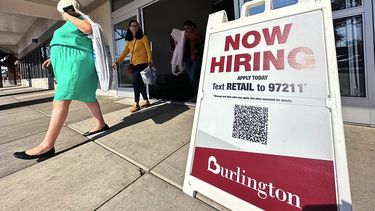 Varias personas salen de una tienda de la cadena minorista Burlington, en cuya entrada un letrero indica la búsqueda de empleados.