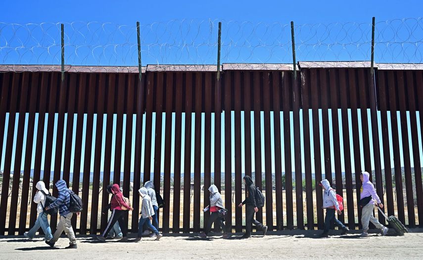 Inmigrantes caminan junto al muro fronterizo con Estados Unidos del lado de territorio de México.