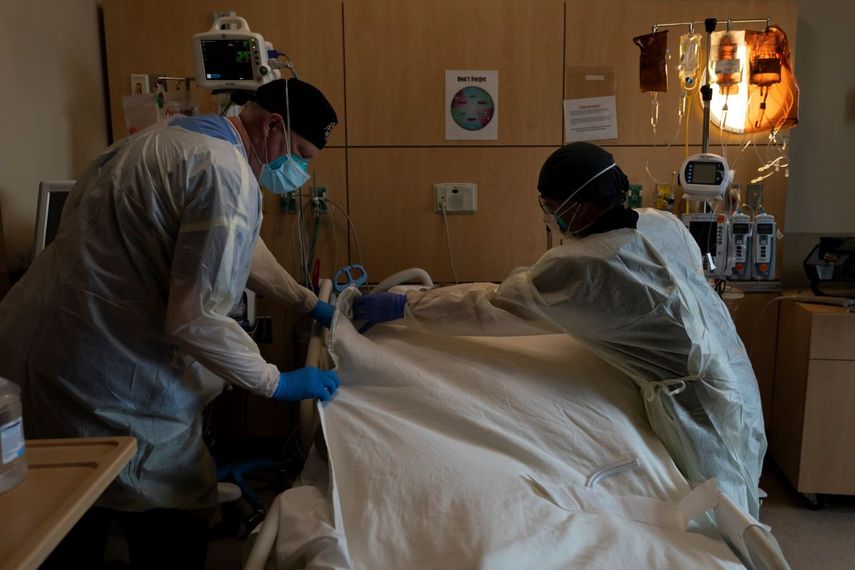 El neumólogo Frans Oudenaar, a la izquierda, y el enfermero Bryan Hofilena cubren el cuerpo de un paciente con COVID-19 con una sábana.