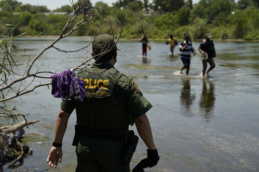 Inmigrantes cruzan el Río Bravo ante la mirada de un agente de Inmigración.