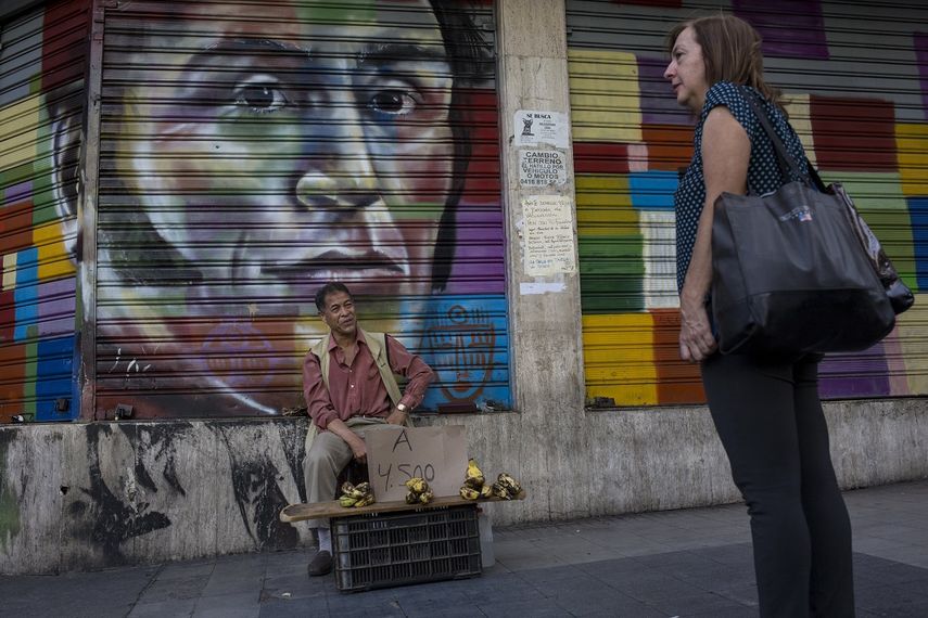 Un vendedor callejero ofrece bananas frente a una pintura con la imagen del líder independentista venezolano Simón Bolívar en Caracas, Venezuela, el martes 16 de julio de 2019.