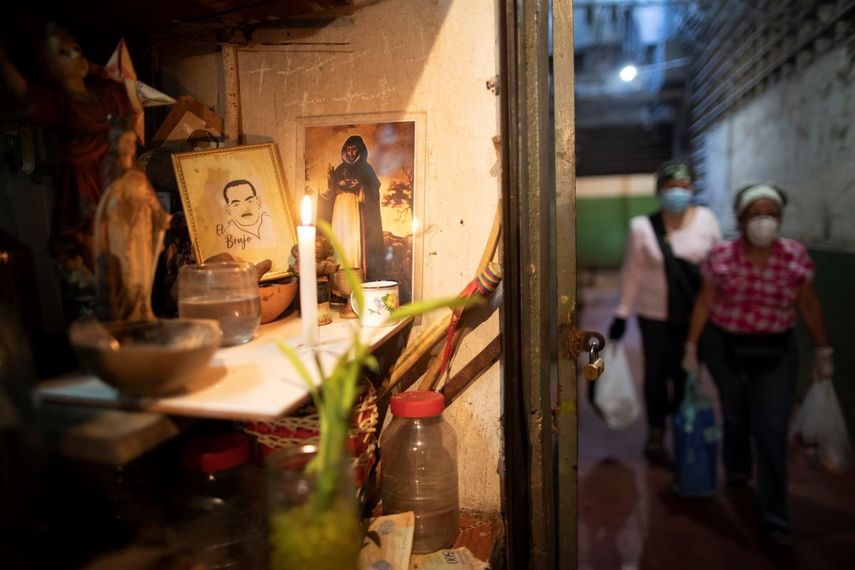 En esta foto del 20 de marzo de 2020, una vela ilumina un altar en un puesto de hierbas en un mercado en Caracas, Venezuela. Ante la llegada del coronavirus algunos venezolanos recurren a plantas como el toronjil, el hinojo y el limoncillo, y frutos como el limón, alegando que eso los ayuda a mejorar el sistema inmunológico y protegerse de la pandemia. Médicos y organizaciones científicas sostienen que el consumo de bebedizos de hierbas no sirve para prevenir ni tratar la enfermedad. 