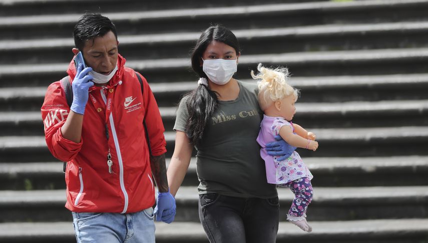 Una pareja con mascarillas y guantes para evitar el contagio del nuevo coronavirus camina de la mano por el centro de Quito, Ecuador, el viernes 10 de abril de 2020.&nbsp;
