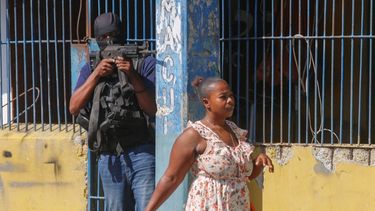 Una mujer pasa junto a un oficial de la Policía Nacional de Haití que custodia la Penitenciaría Nacional, en el centro de Puerto Príncipe, el jueves 14 de marzo de 2024.