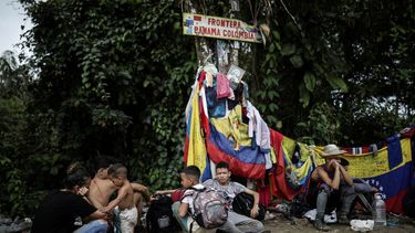 Migrantes sentados bajo un cartel que marca la frontera entre Panamá y Colombia durante su viaje a través del Tapón del Darién.