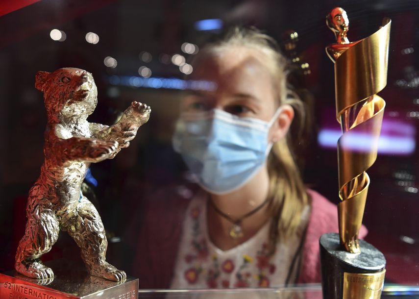 En esta foto del 14 de mayo de 2020, una chica con mascarilla mira un Oso de Oro de la Berlinale y un Lola durante la exposición Traumfabrik, 100 años de cine en Babelsberg en Berlín. El Festival Internacional de Cine de Berlín anunció el jueves las 15 películas que conformarán la competencia este año.