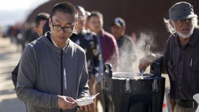 Un chino recibe avena cocida de manos de un voluntario mientras aguarda junto con otras personas a solicitar asilo tras cruzar la frontera con México, el martes 24 de octubre de 2023, cerca de Jacumba, California.