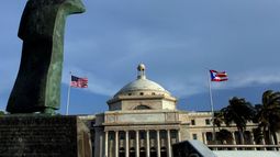 &nbsp;Una estatua de bronce de San Juan Bautista frente al Capitolio, flanqueada por banderas de Estados Unidos y Puerto Rico, en San Juan, Puerto Rico.&nbsp;