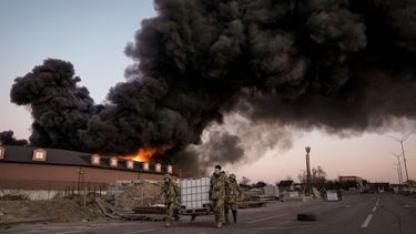 Militares ucranianos transportan unos contenedores y como telón de fondo un incendio en un almacén tras un bombardeo el jueves 17 de marzo de 2022, en las afueras de Kiev (Ucrania).
