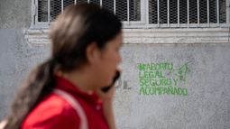 Una mujer usa su teléfono móvil mientras pasa frente a un grafiti a favor de la legalización del aborto pintado por organizaciones feministas en Caracas, Venezuela.