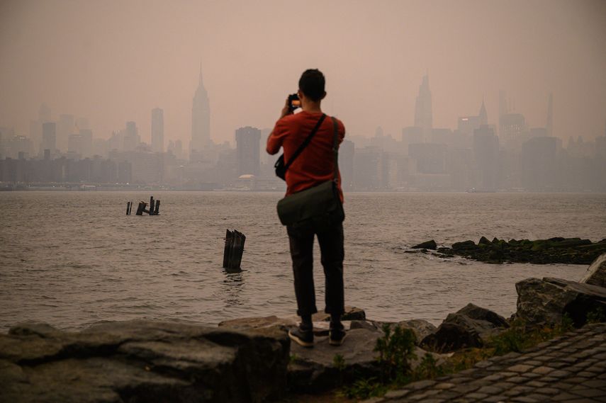 Un hombre frente al horizonte de la ciudad de Nueva York y el East River envueltos en humo, en Brooklyn el 6 de junio de 2023, a causa de los incendios en Canadá.&nbsp; &nbsp;