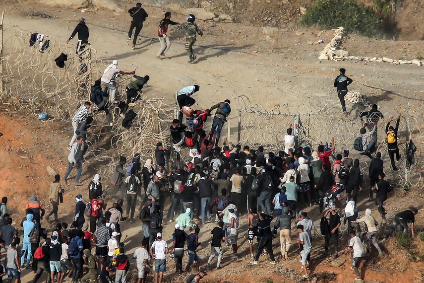 Migrantes asaltan una valla de alambre de púas mientras intentan cruzar la frontera terrestre con el enclave africano español de Ceuta, cerca de Fnideq, en el norte de Marruecos, el 15 de septiembre.