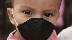 Gael G&oacute;mez, de un a&ntilde;o, usa una mascarilla para protegerse del nuevo coronavirus mientras su madre lo sostiene para pedir comida en la Carretera de Oro en Ilopango, El Salvador, el martes 19 de mayo de 2020.