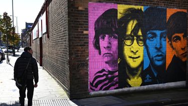 Los peatones pasan por un mural que representa a los miembros de la banda de rock británica The Beatles: Ringo Starr, John Lennon, Paul McCartney y George Harrison en el costado de un edificio en Liverpool, noroeste de Inglaterra, el 13 de octubre de 2020.