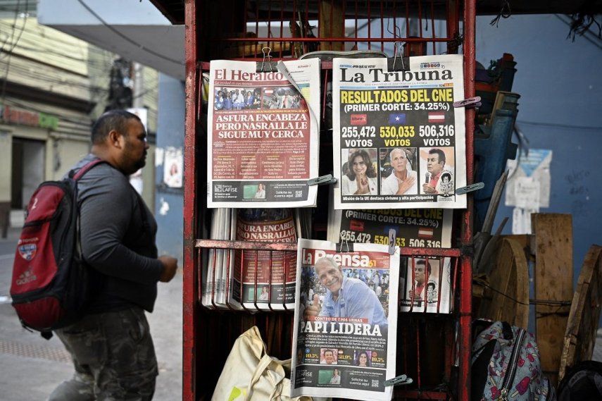 Un hombre pasa junto a un quiosco con las portadas de periódicos en Tegucigalpa, el 1 de diciembre de 2025, al día siguiente de las elecciones nacionales.nado. &nbsp; &nbsp;