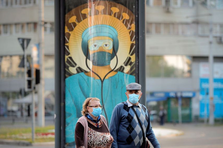 Ancianos con mascarillas pasan frente a una pintura de un empleado m&eacute;dico con equipo protector al estilo del Cristo Pantocr&aacute;tor en Bucarest, Rumania, el mi&eacute;rcoles 29 de abril de 2020.&nbsp;