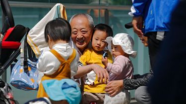 Un anciano juega con niños cerca de un edificio de oficinas en Beijing, el 10 de mayo de 2021. El gobierno chino relajará los límites de natalidad para permitir que todas las parejas puedan tener tres hijos en lugar de dos para hacer frente al rápido envejecimiento de la población, según dijo el lunes 31 de mayo una agencia estatal de noticias.