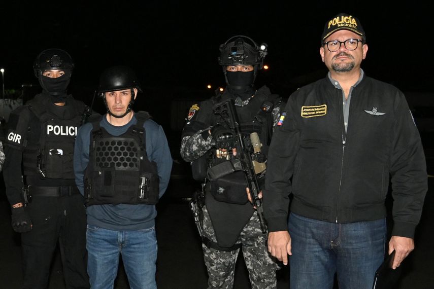 Agentes de la policía ecuatoriana, junto al ministro del Interior, John Reimberg (derecha), posan con el narcotraficante ecuatoriano Ángel Aguilar (centro), alias «Lobo Menor», a su llegada a las instalaciones aeropoliciales del aeropuerto de Guayaquil el 19 de marzo de 2026.