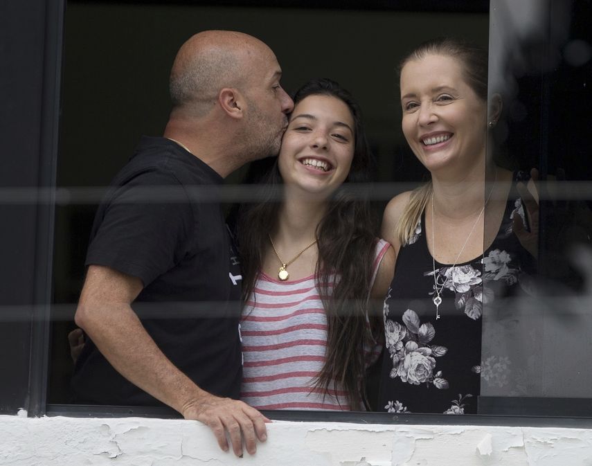 En esta imagen del 20 de septiembre de 2014 se ve a Iván Simonovis, exjefe de la policía de Caracas, mientras le da un beso a su hija Ivana, a un costado de su esposa Bony, mientras se asoman por una ventana en su residencia de Caracas, Venezuela, en donde pasó casi cinco años bajo arresto domiciliario.