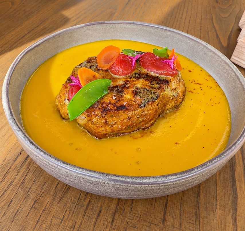 Una salsa de color intenso rodea el pescado servido en el plato, terminado con vegetales y flores.