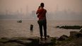 Un hombre frente al horizonte de la ciudad de Nueva York y el East River envueltos en humo, en Brooklyn el 6 de junio de 2023, a causa de los incendios en Canadá.&nbsp; &nbsp;