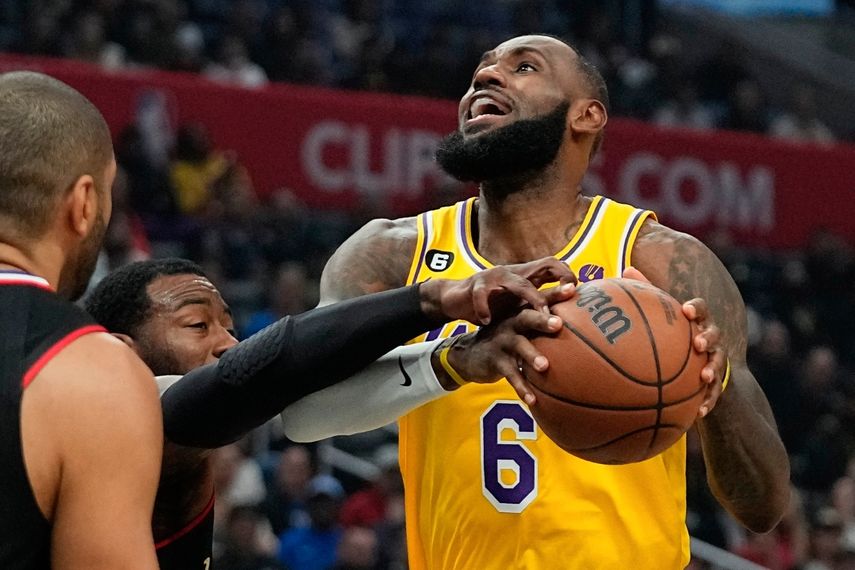 El alero de los Lakers de Los Ángeles, LeBron James, a la derecha, intenta disparar mientras recibe una falta del escolta de los Clippers de Los Ángeles, John Wall