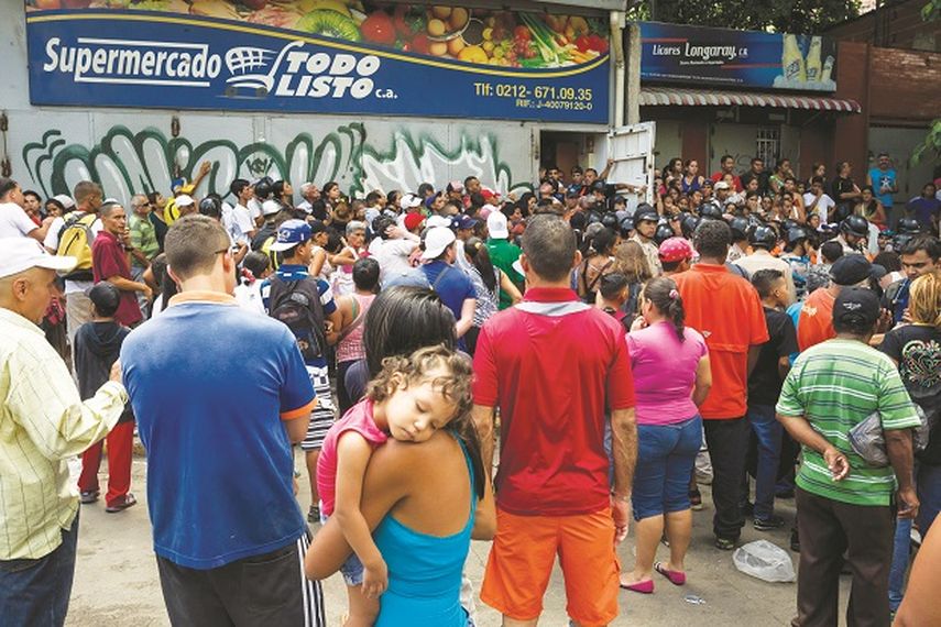 Miembros de la fuerza policial trata de contener a un grupo de personas que intentan entrar a un supermercado en Caracas. (EFE)