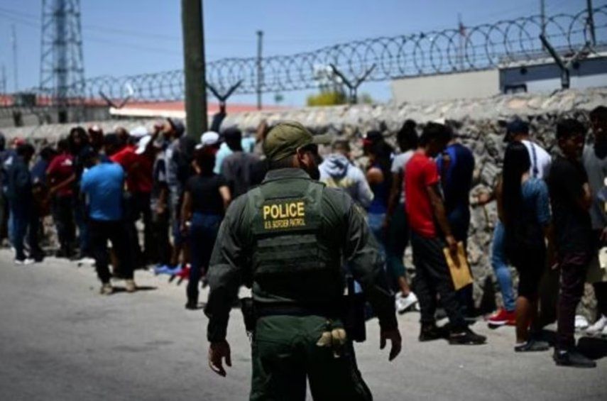 Un policía de fronteras camina junto a una fila de migrantes en un puesto fronterizo de la ciudad tejana de El Paso tras cruzar la frontera mexicana, el 9 de mayo de 2023 al sur de EEUU. El Programa Movilidad Segura busca una entrada controlada a Estados Unidos