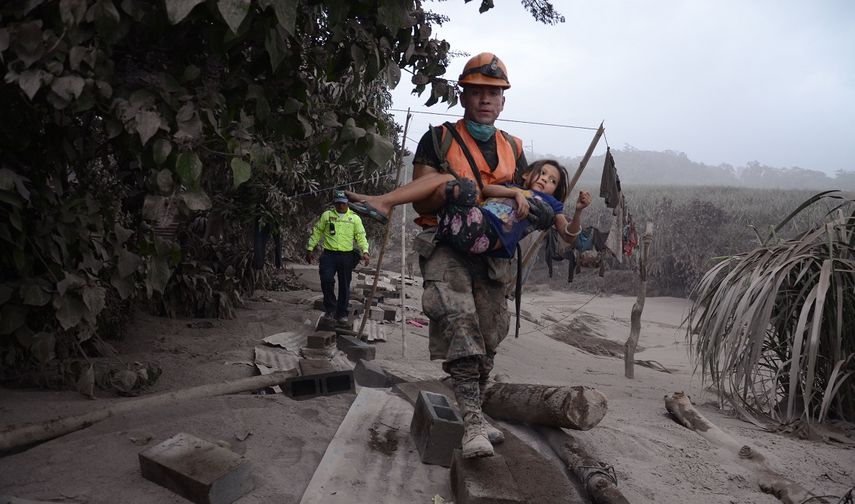 Un trabajador de los equipos de rescate de Guatemala ayuda a una niña tras la erupción del Volcán de fuego en Guatemala, el 3 de junio de 2018.