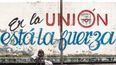 Una señora sentada frente a un cartel en Cuba.&nbsp;