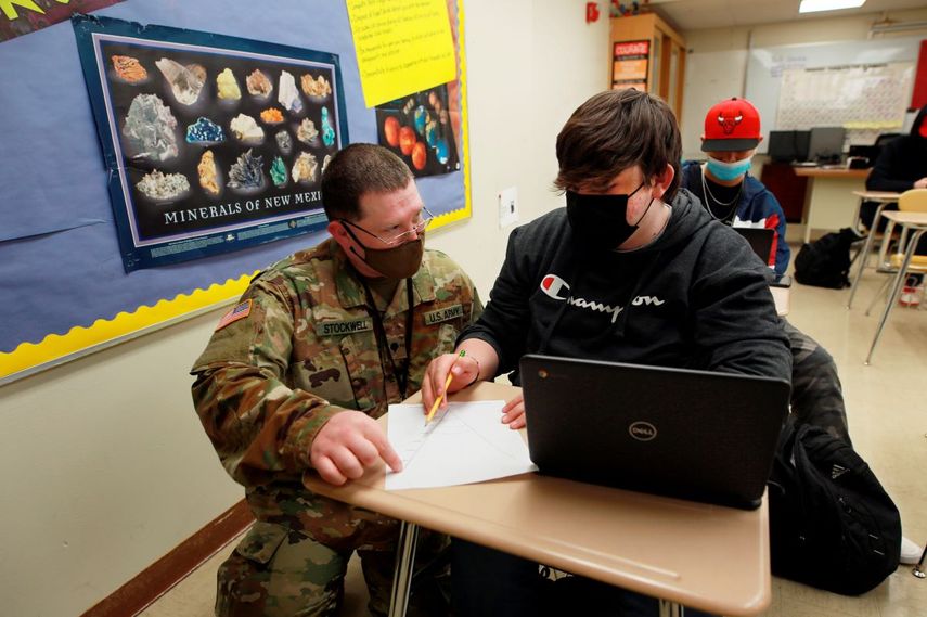 El especialista de la Guardia Nacional de Nuevo México Michael Stockwell, de rodillas mientras ayuda al alumno de secundaria Alamogordo Aiden Cruz con una tarea de geología, en la Escuela Secundaria de Alamogordo, el martes 8 de febrero de 2022 en Alamogordo, Nuevo México.