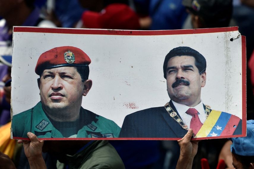 Partidario del Régimen sostiene folleto con los retratos de Hugo Chávez y Nicolás Maduro, mientras participa durante una marcha en Venezuela