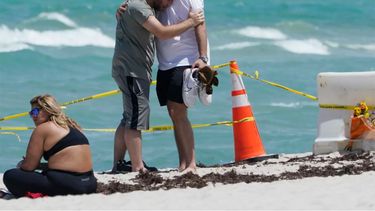Dos jóvenes se abrazan y se consuelan, mientras una joven mira de reojo el derrumbe del edificio, en Surfise, al norte de Miami Beach.