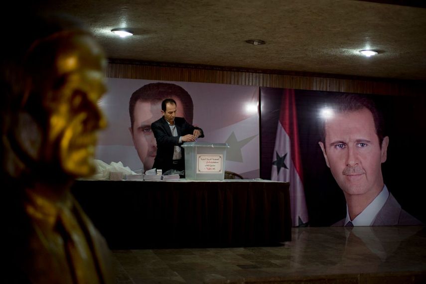 En esta imagen de archivo del 13 de abril de 2016, un funcionario sirio espera a los votantes en un centro electoral, junto a carteles del presidente, Bashar Assad, durante las elecciones parlamentarias en Damasco, Siria.&nbsp;