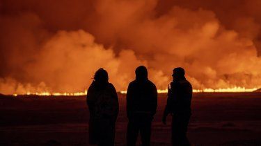Gente observando el cielo nocturno iluminado por la erupción de un volcán en Grindavik, en la península islandesa de Reykjanes, el lunes 18 de diciembre de 2023.&nbsp;